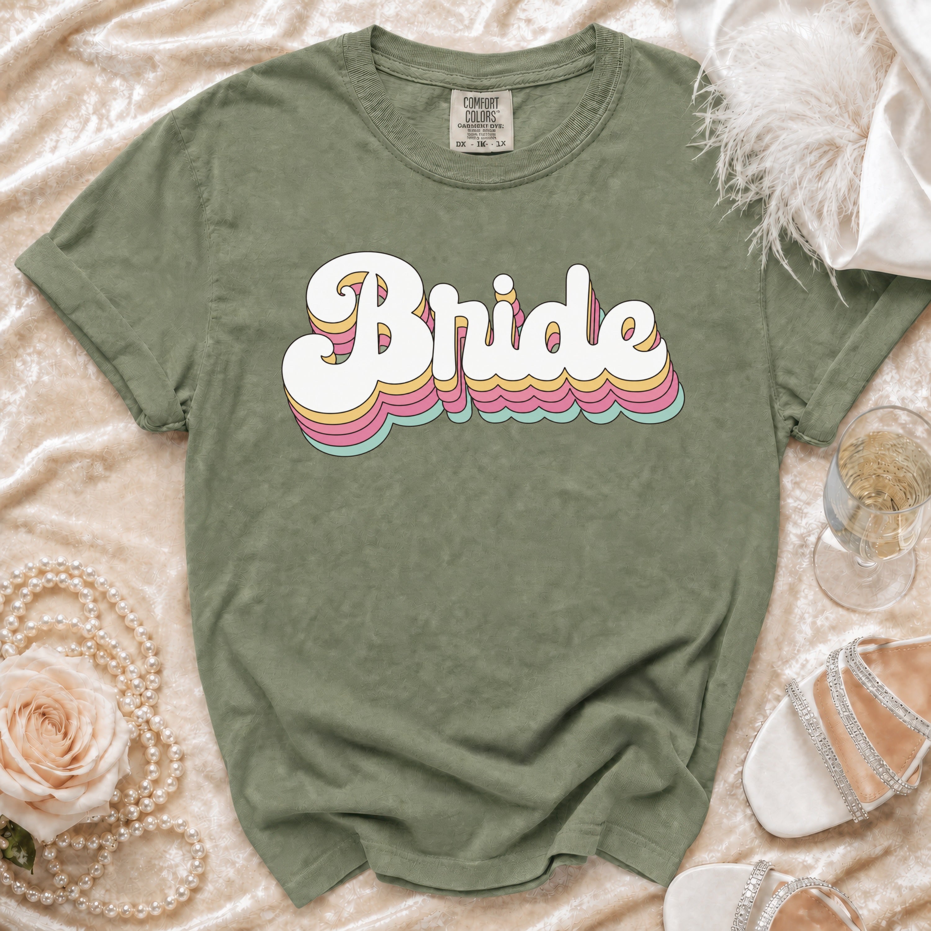 Sage green t-shirt with "Bride" in retro stacked lettering and wedding accessories.