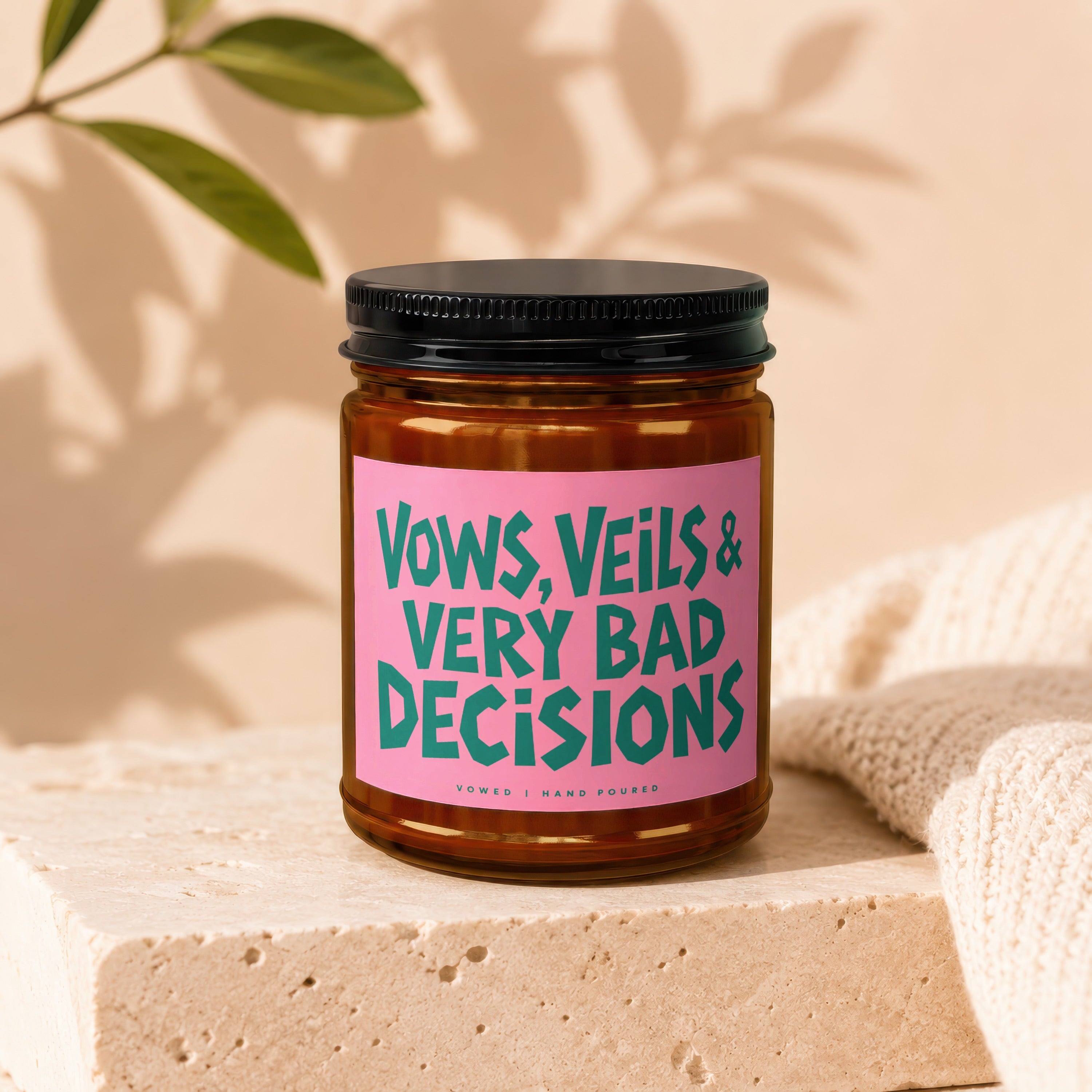 Brown glass candle with pink label reading "Vows, Veils & Very Bad Decisions."