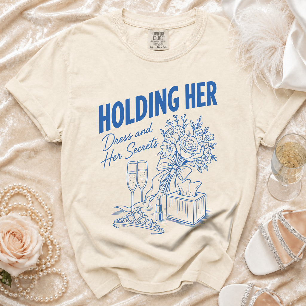 Cream t-shirt with blue graphic saying "HOLDING HER Dress and Her Secrets".