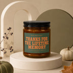 Amber candle with "Thanks for the lifetime memory" text in an autumnal setting.