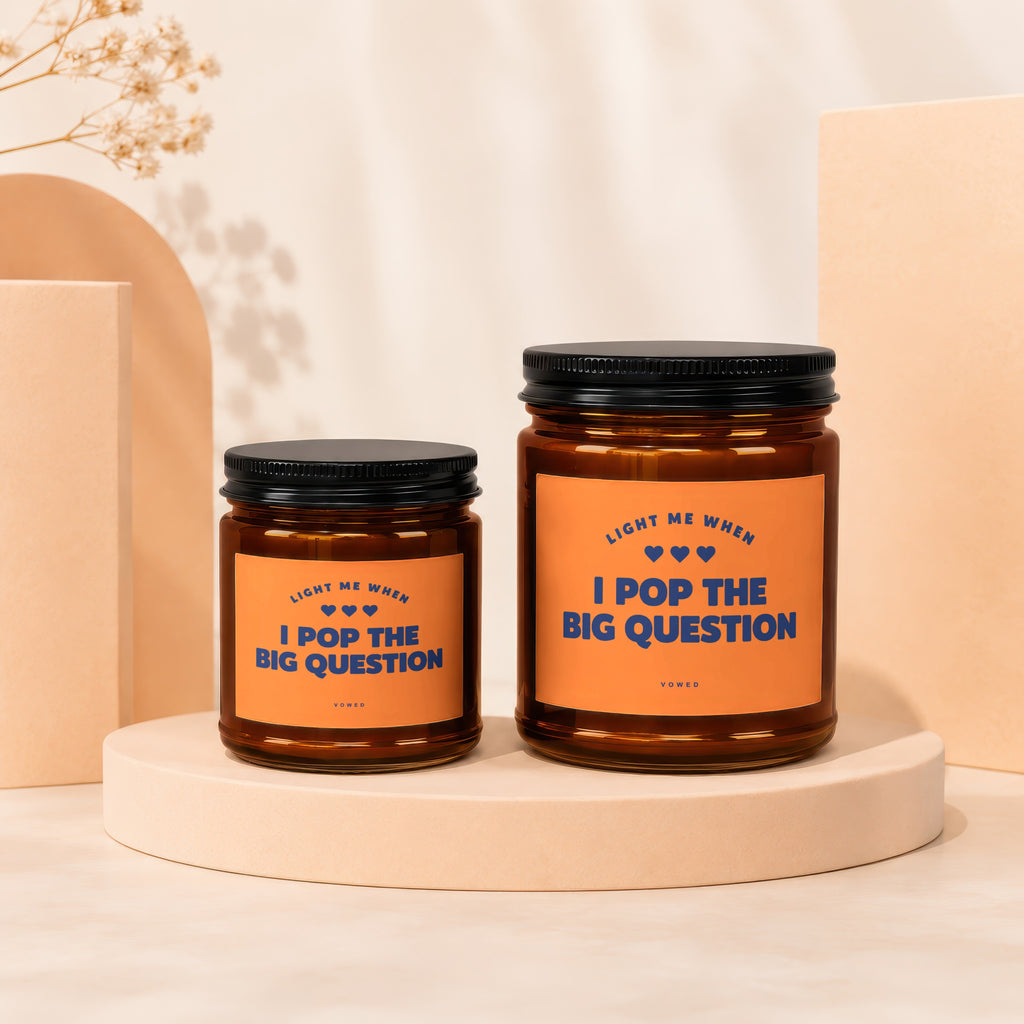 Two amber glass candles with orange labels that read "Light me when I pop the big question".