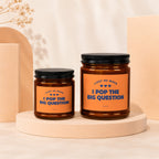 Two amber glass candles with orange labels that read "Light me when I pop the big question".