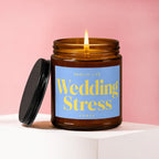 Amber jar candle with lit flame, "Smells Like Wedding Stress" label, lid to the side.