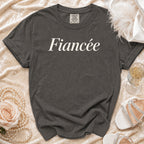 Dark grey t-shirt with "Fiancée" text, pearls, rose, champagne, and heels.