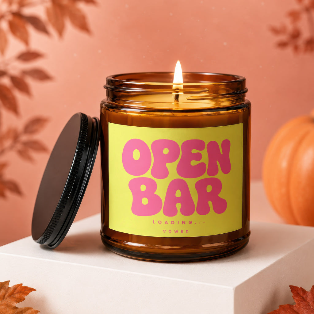 Amber jar candle with bright yellow label reading "OPEN BAR LOADING... VOWED".