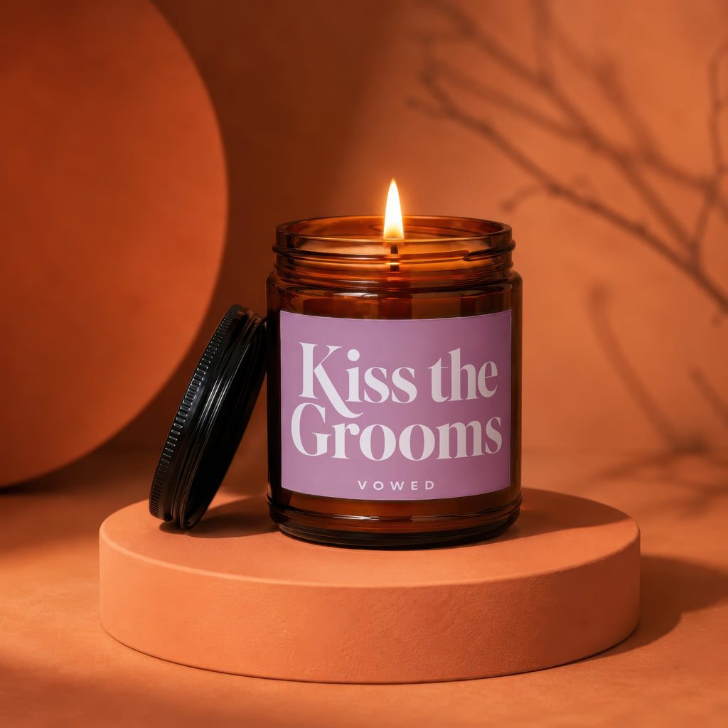 Amber glass candle with lit flame, "Kiss the Grooms" label, VOWED.