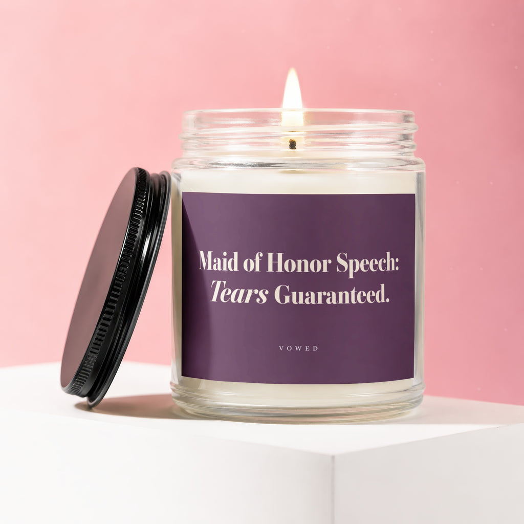 Glass candle with lit wick, black lid, and purple label reading "Maid of Honor Speech: Tears Guaranteed."