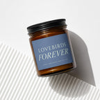 Amber glass candle with "Lovebirds Forever" text on blue label.
