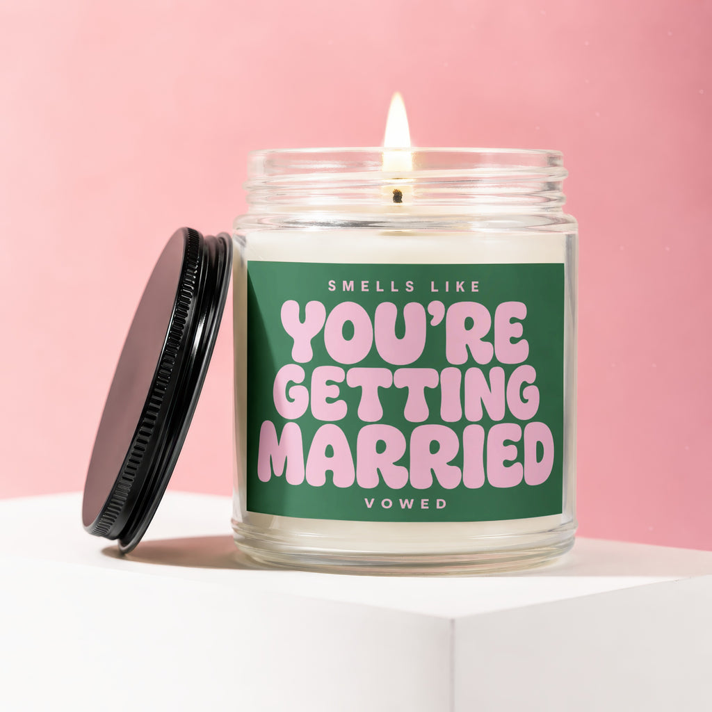 Glass candle with burning wick, label reads "Smells like You're Getting Married"