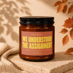 Amber candle with "We Understood The Assignment" text on label.
