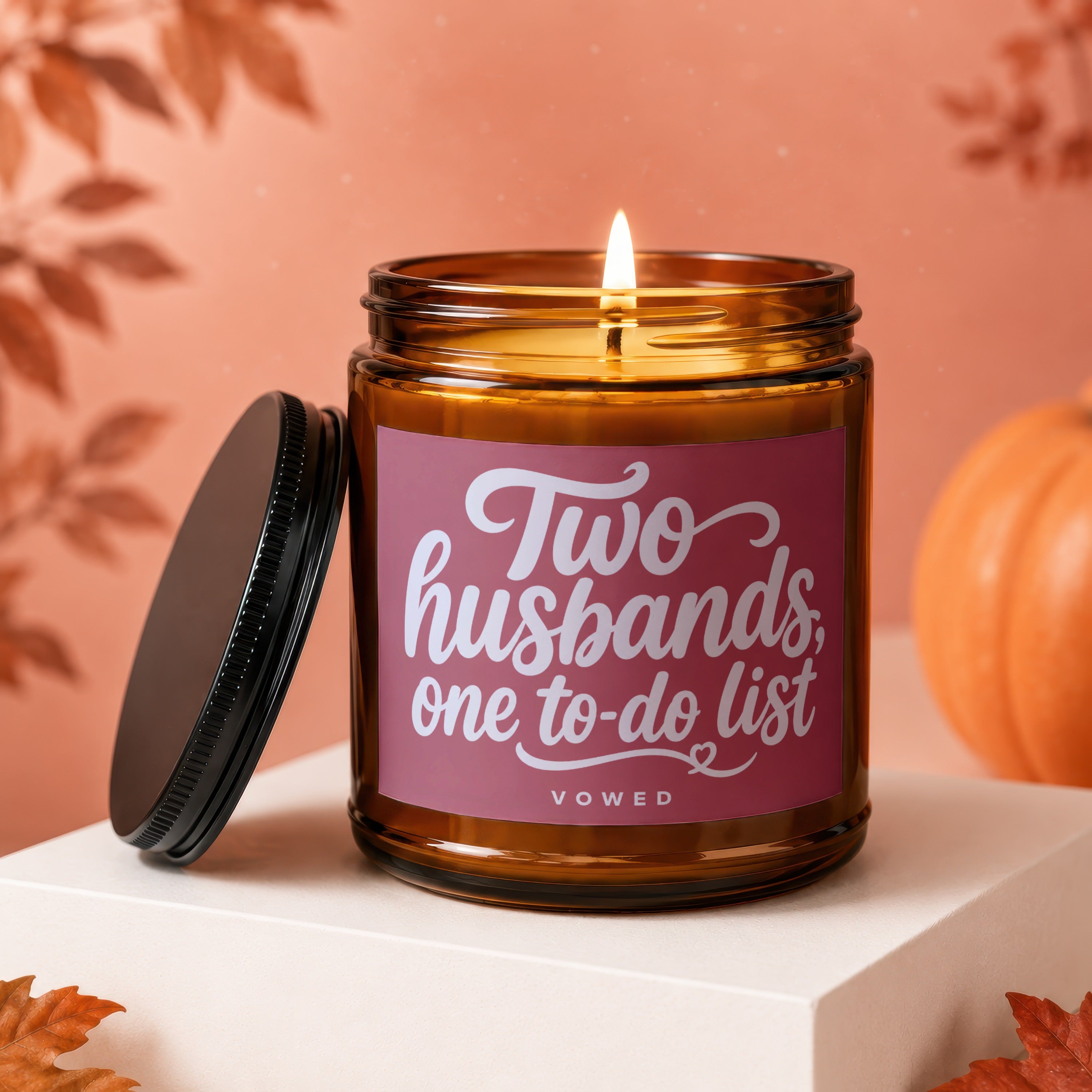 Amber jar candle with lit wick, text "Two husbands, one to-do list" and "VOWED".