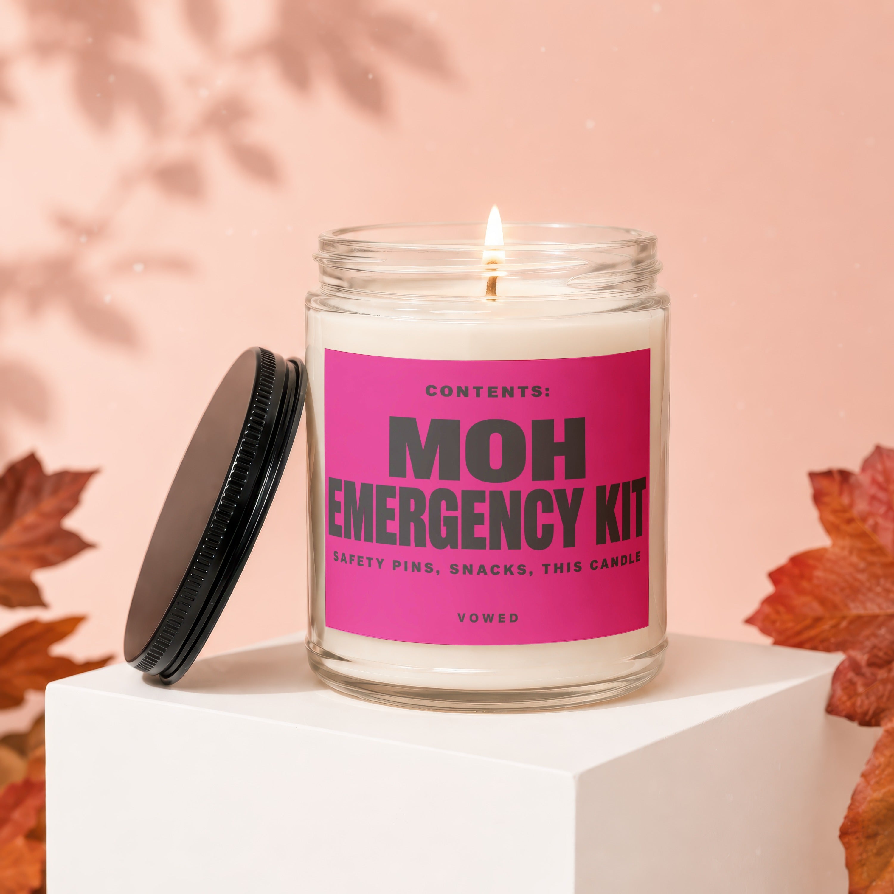 Lit candle in glass jar labeled "MOH EMERGENCY KIT", with lid off.