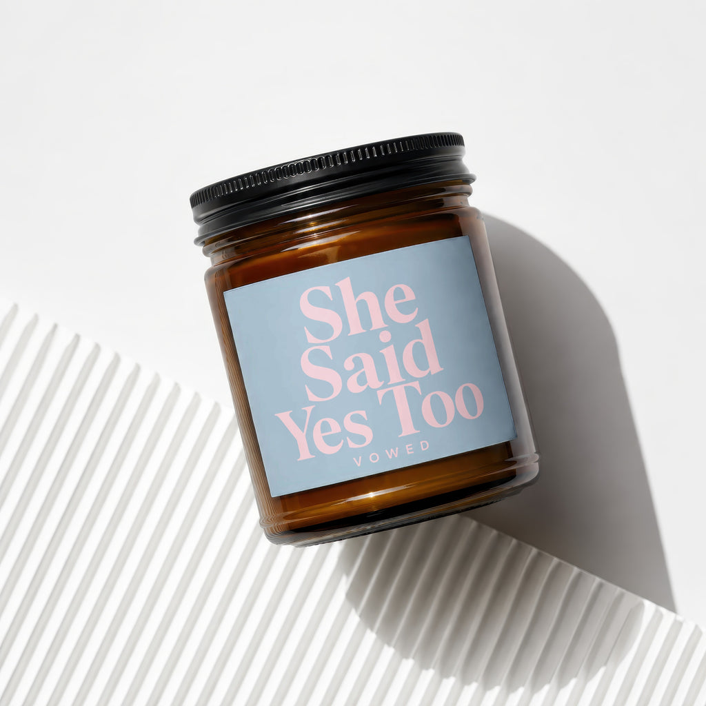 Brown glass jar candle with a blue label reading "She Said Yes Too, VOWED".