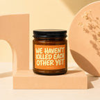 Amber jar candle with orange label that reads "WE HAVEN'T KILLED EACH OTHER YET"