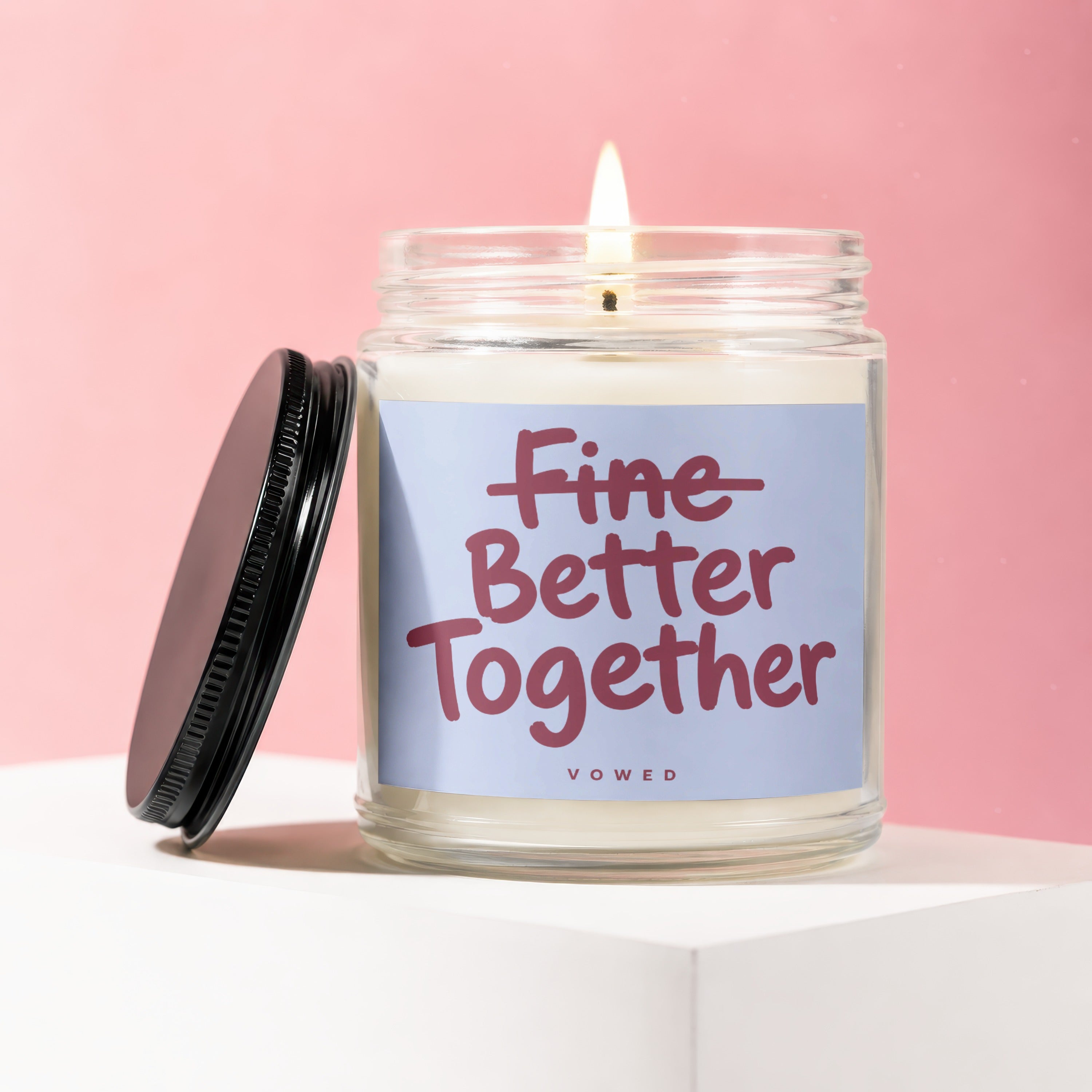 Glass candle with lid off, flame lit, and text "Fine Better Together"