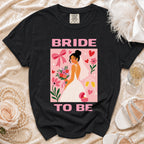 Black t-shirt with "Bride To Be" text and a bride illustration with flowers and champagne.