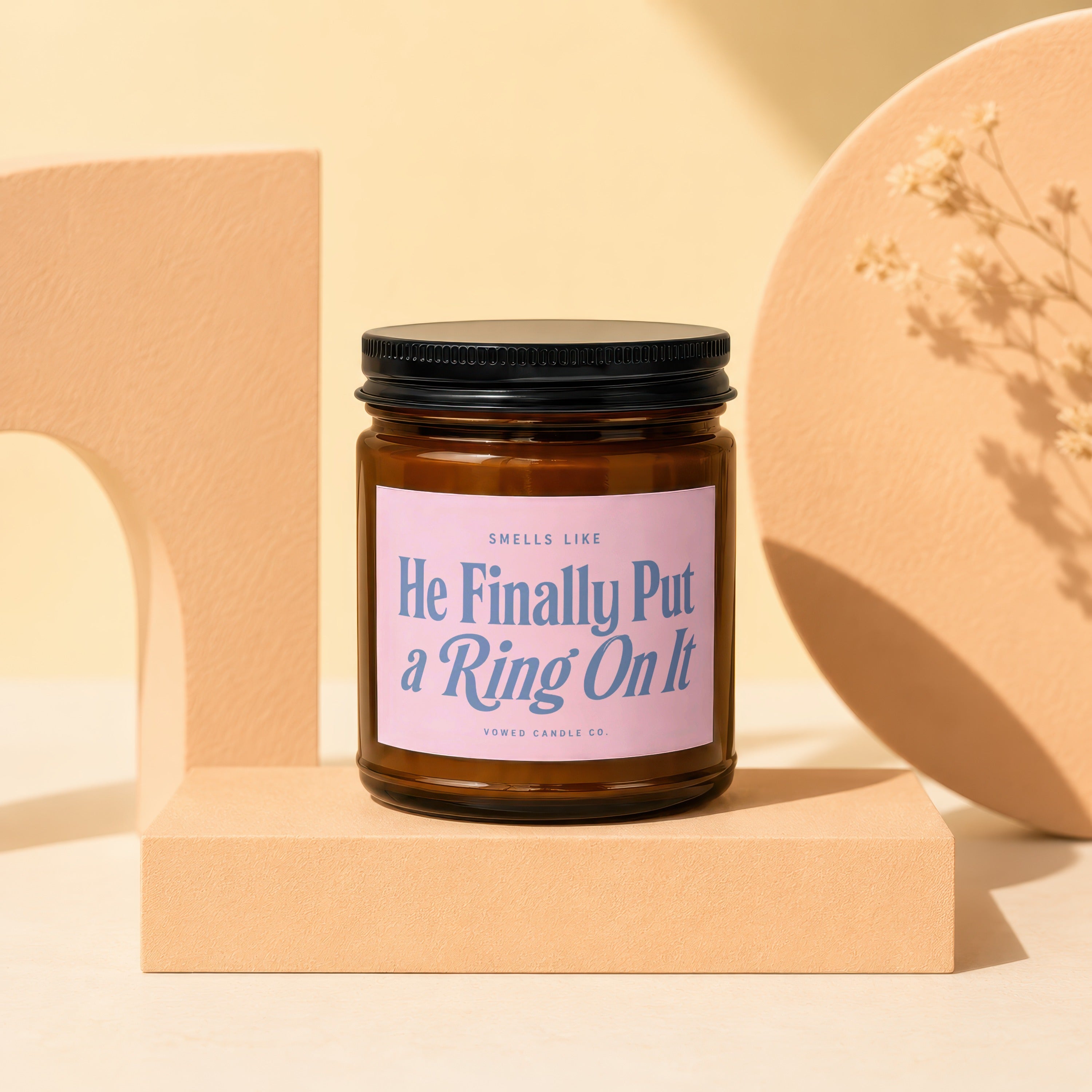 Brown candle with pink label saying "He Finally Put a Ring On It" by Vowed Candle Co.