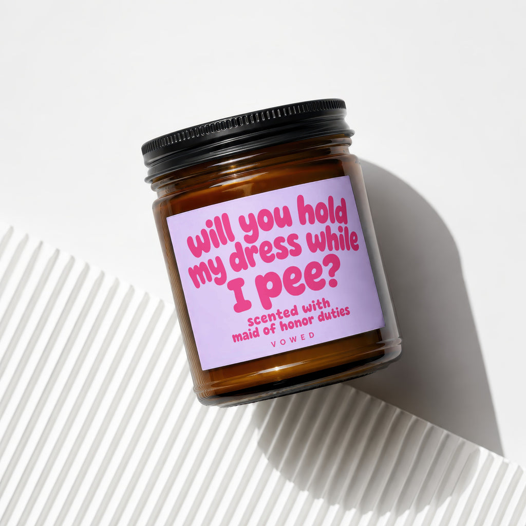 Amber candle with a lavender label reading "will you hold my dress while I pee?".