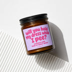 Amber candle with a lavender label reading "will you hold my dress while I pee?".