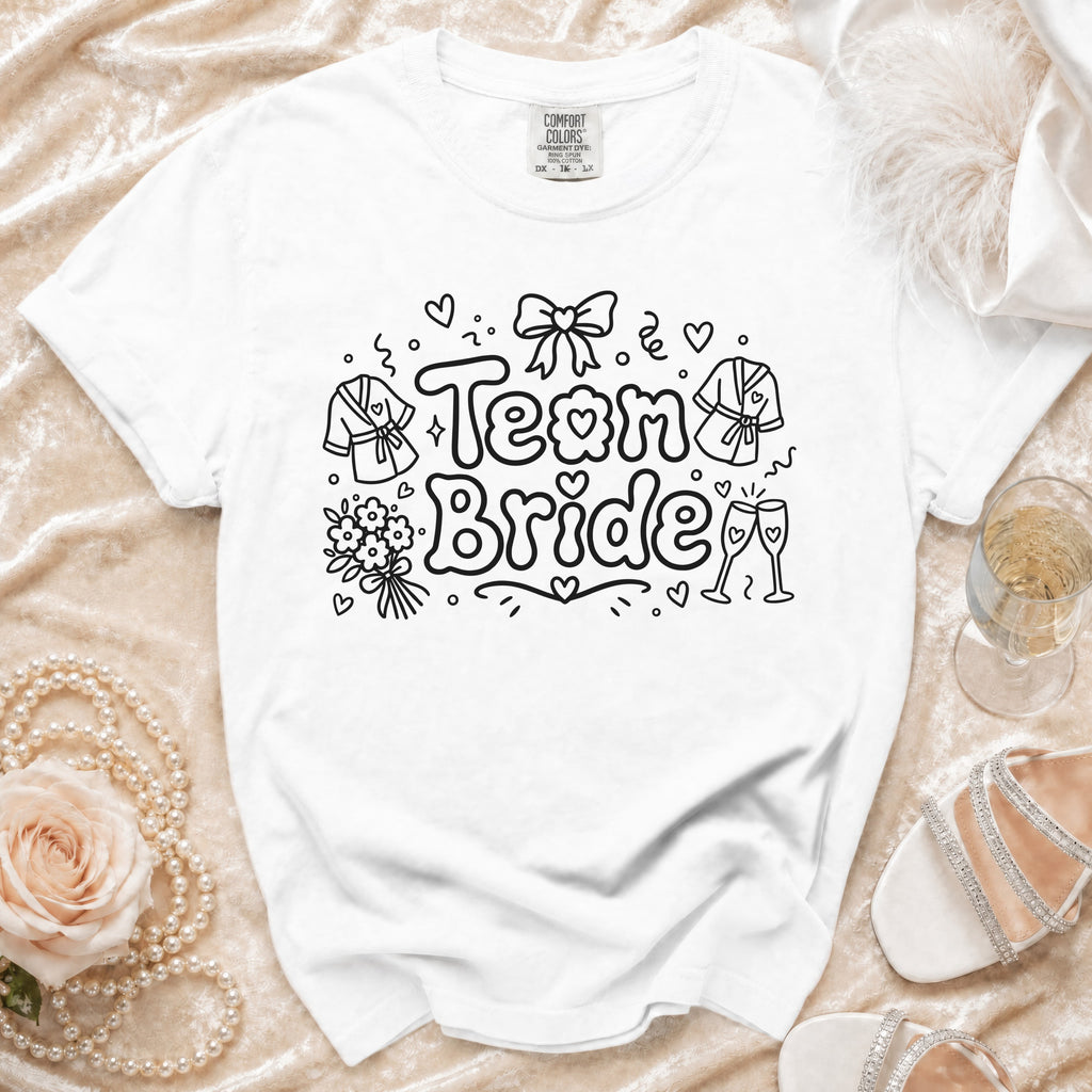 White t-shirt with "Team Bride" graphic, featuring robes, flowers, and champagne glasses.