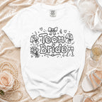 White t-shirt with "Team Bride" graphic, featuring robes, flowers, and champagne glasses.