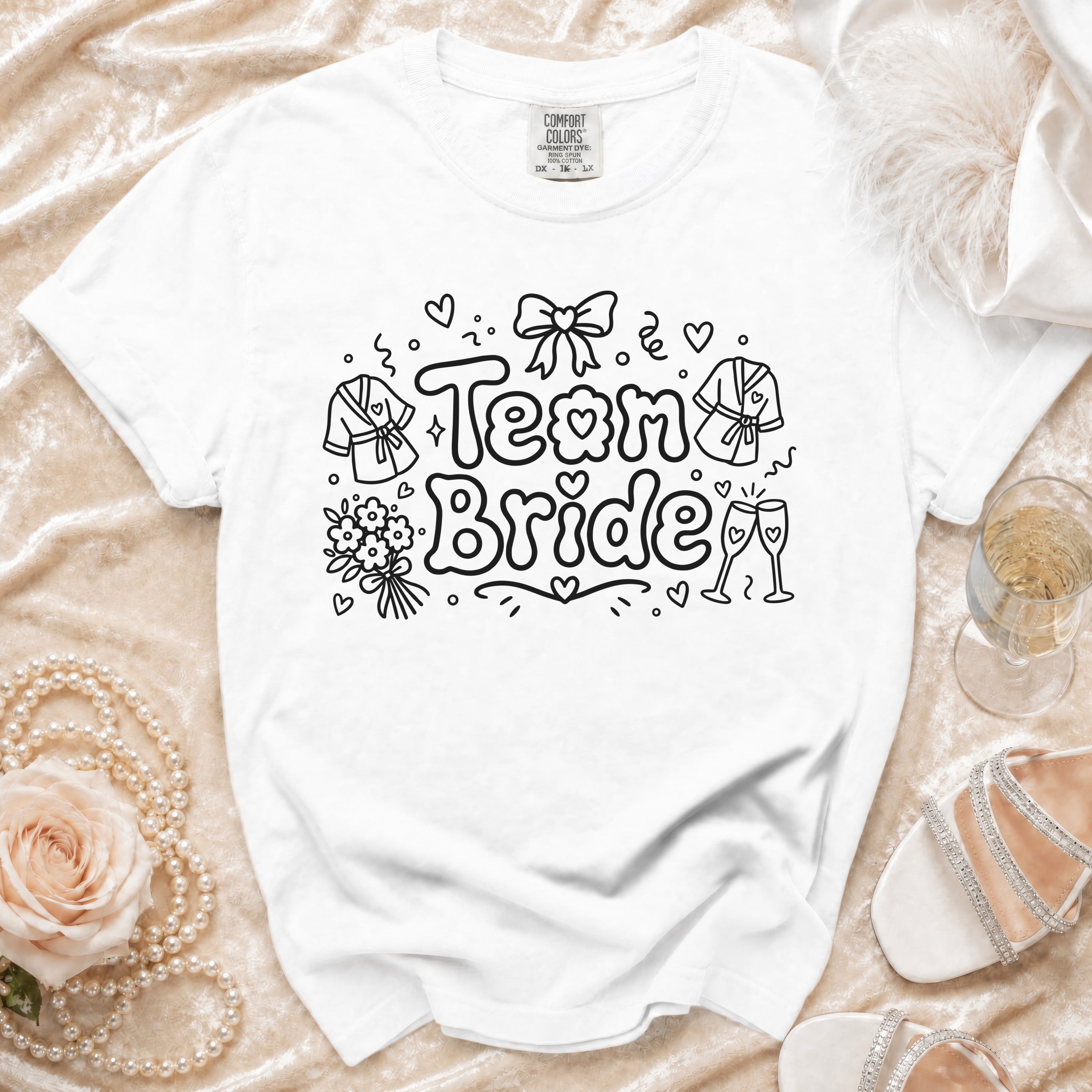 White t-shirt with "Team Bride" graphic, featuring robes, flowers, and champagne glasses.