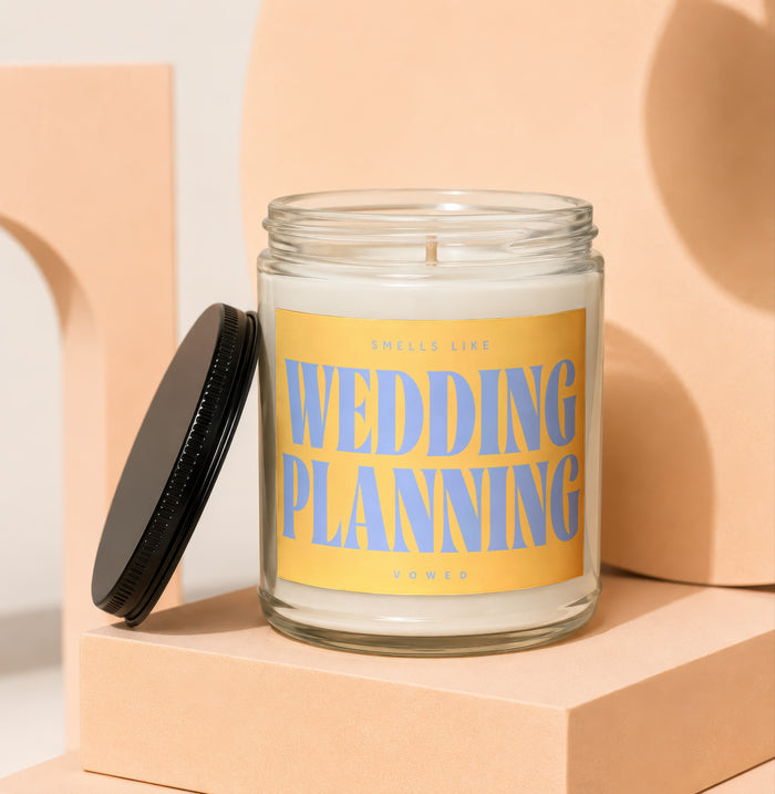 Glass candle with "Smells like Wedding Planning" on yellow label.