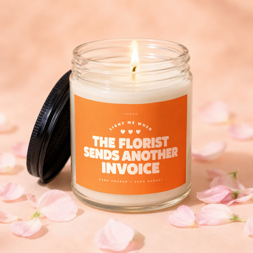 Glass candle with an orange label that reads "VOWED LIGHT ME WHEN THE FLORIST SENDS ANOTHER INVOICE".