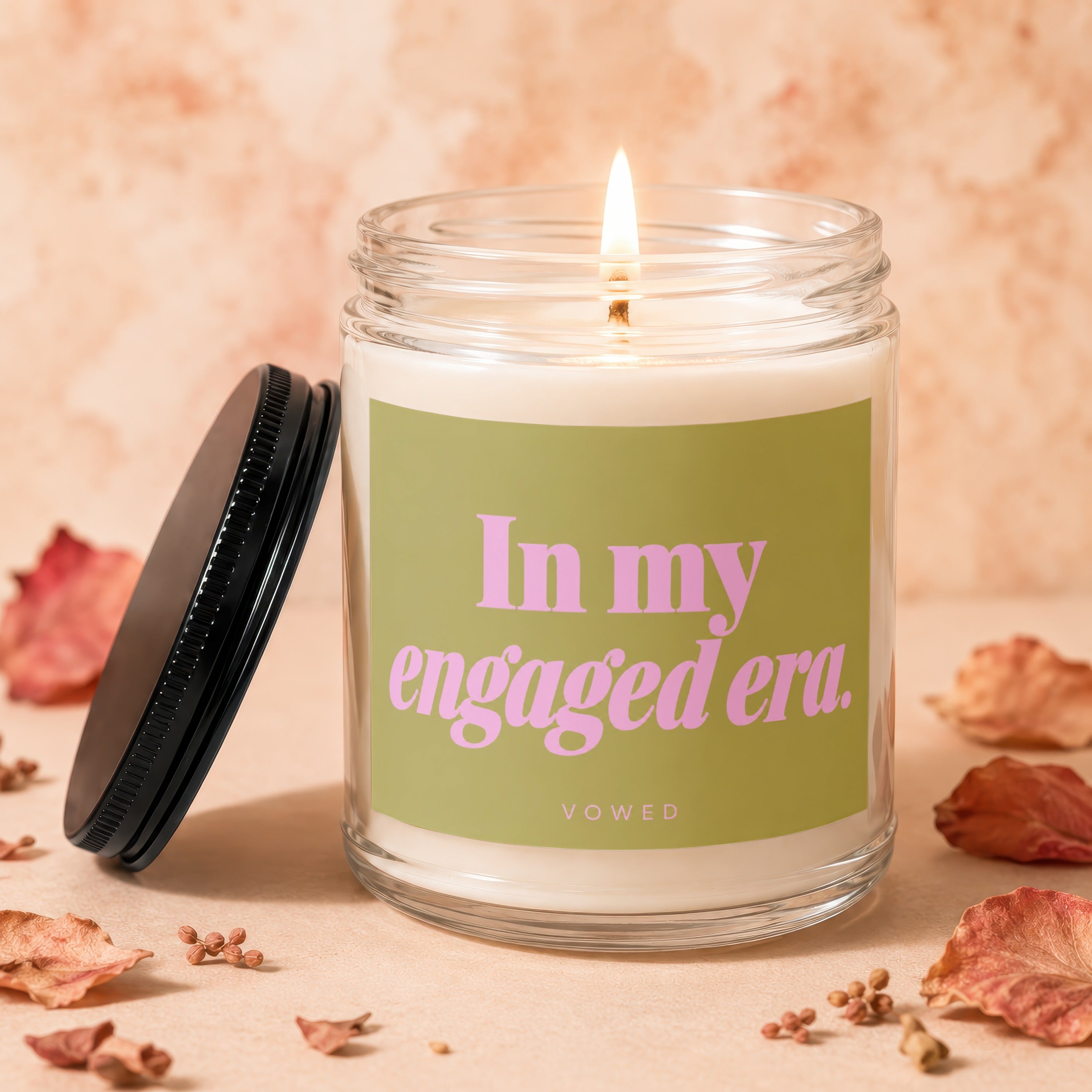 Candle with text "In my engaged era. VOWED" and lit wick.