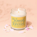 Glass jar candle with yellow label reading "Vowed, forever" and "VOWED" on a pink background.