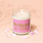 Lit candle with "We Made It to 'I Do'" text on pink label, surrounded by petals.