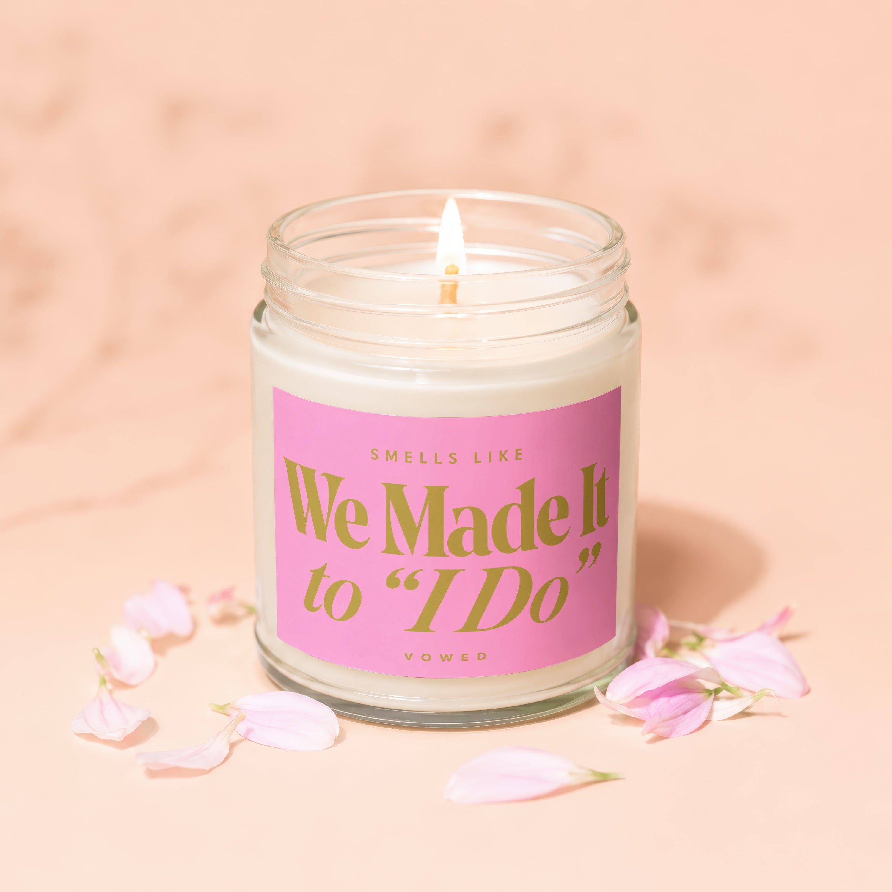 Lit candle with "We Made It to 'I Do'" text on pink label, surrounded by petals.