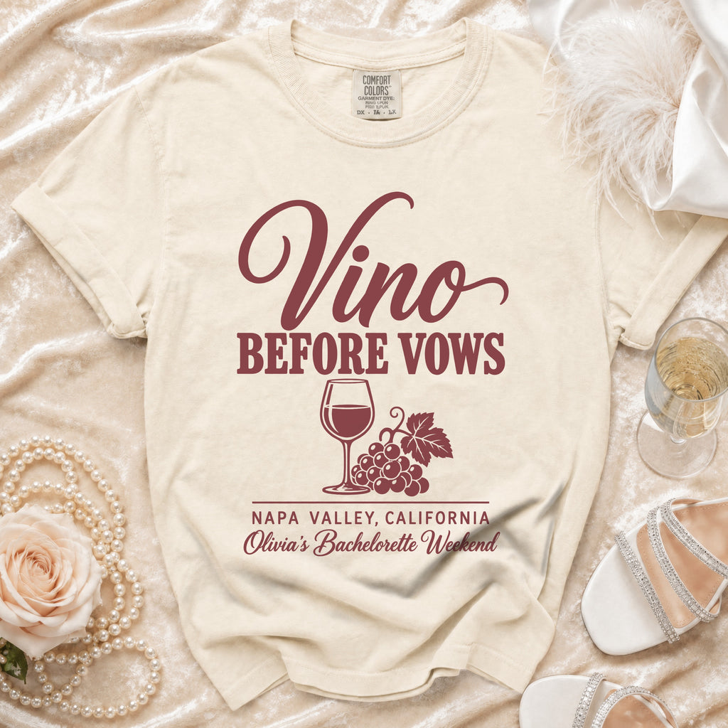 Cream-colored t-shirt featuring the maroon text Vino Before Vows, a wine glass, grapes, and bachelorette weekend details.