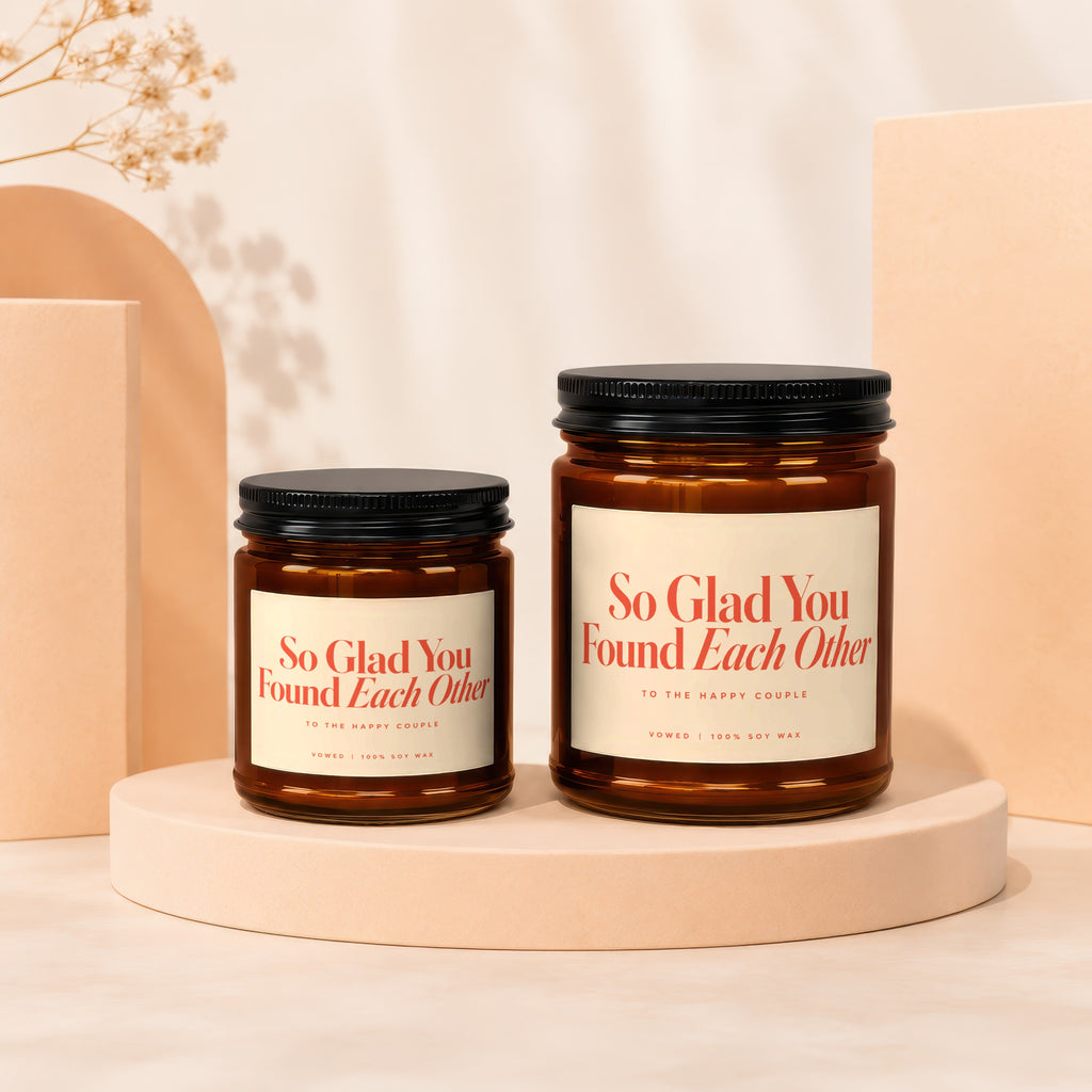 Two amber glass candles with black lids, labeled "So Glad You Found Each Other".