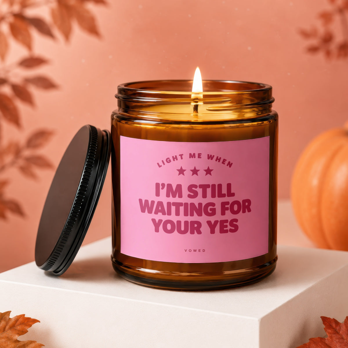 Amber glass candle with pink label reading "Light me when I'm still waiting for your yes".