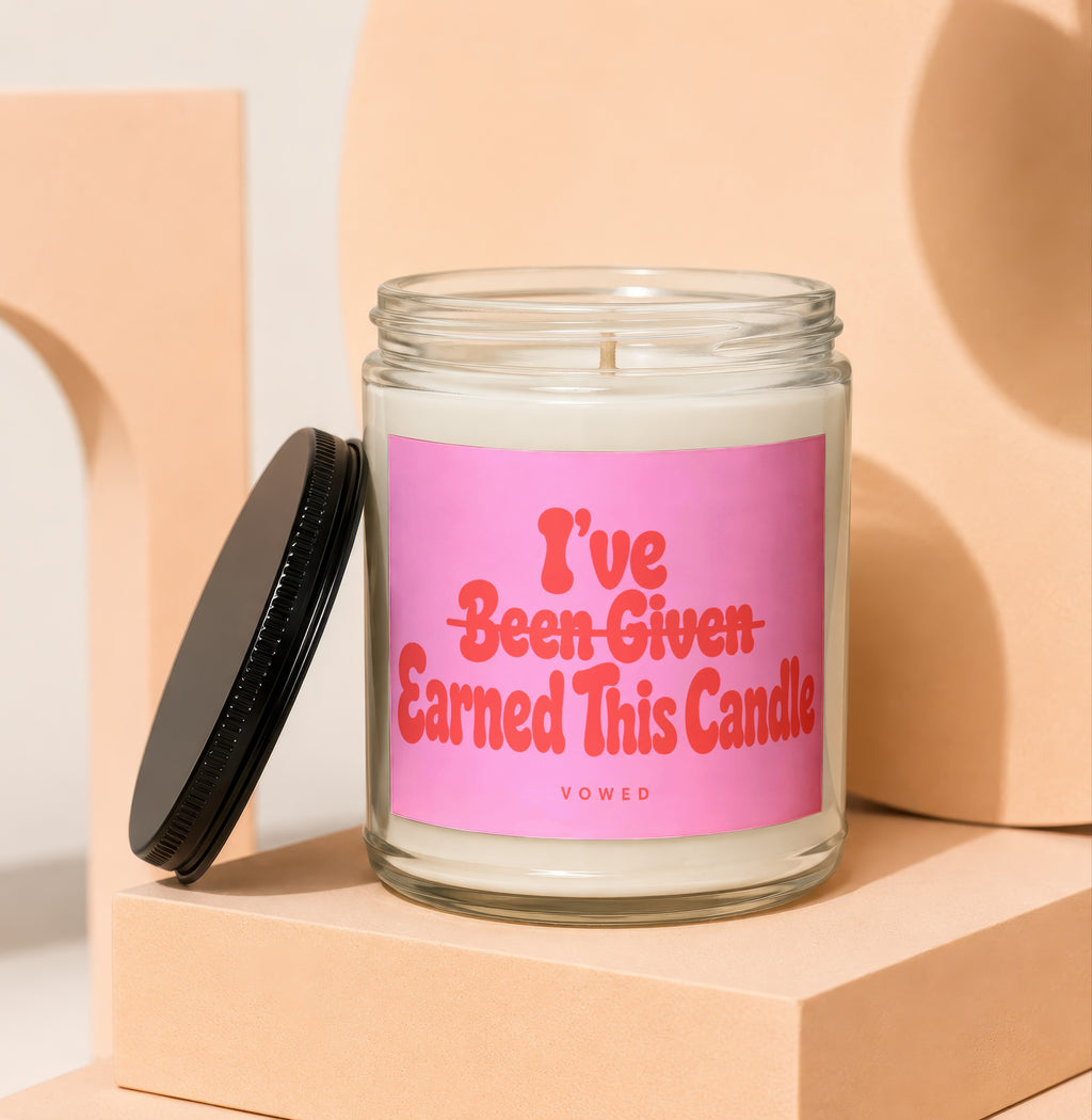Glass candle with pink label reading "I've Been Given Earned This Candle VOWED".