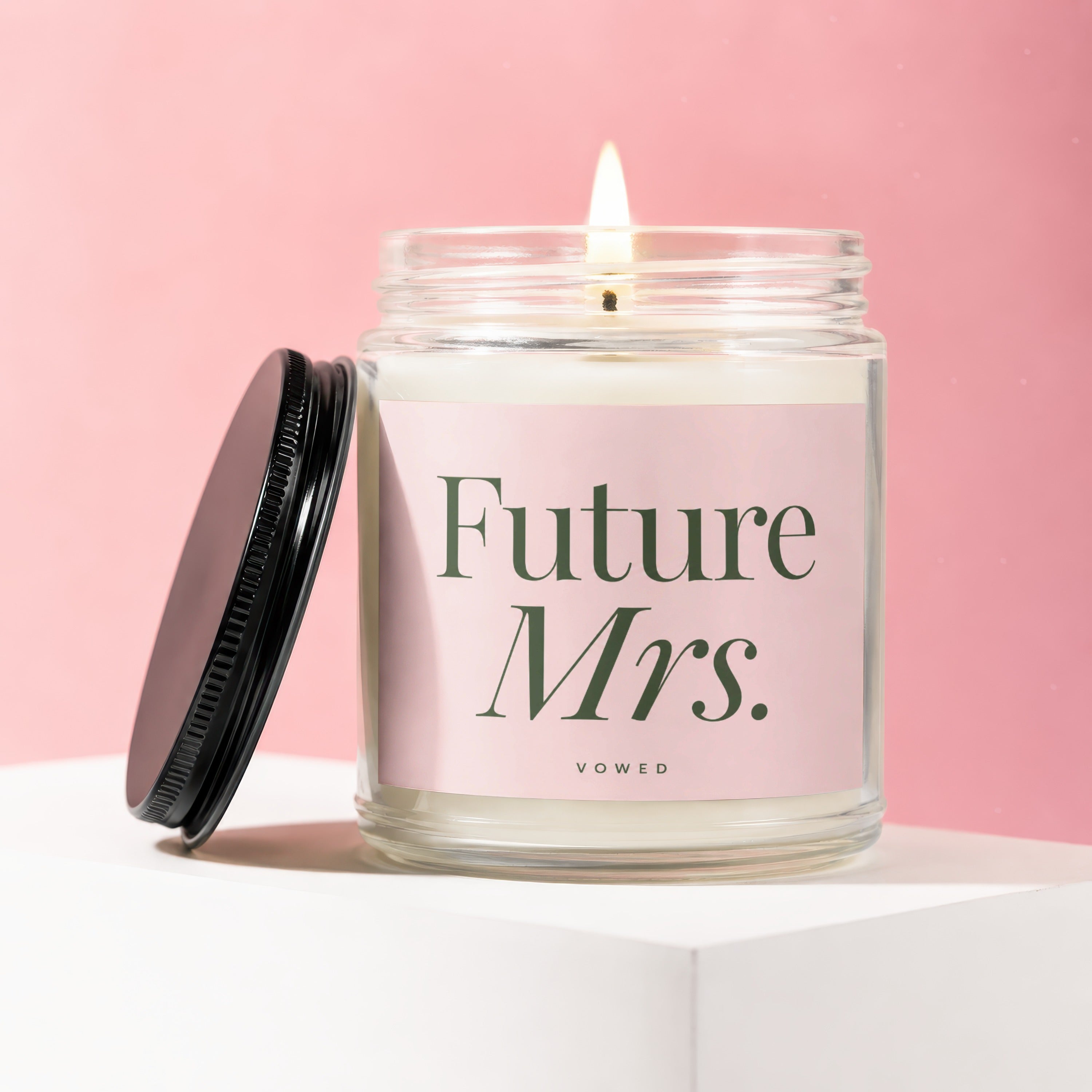 Lit candle in a glass jar with a black lid, labeled "Future Mrs. Vowed" on a pink background.
