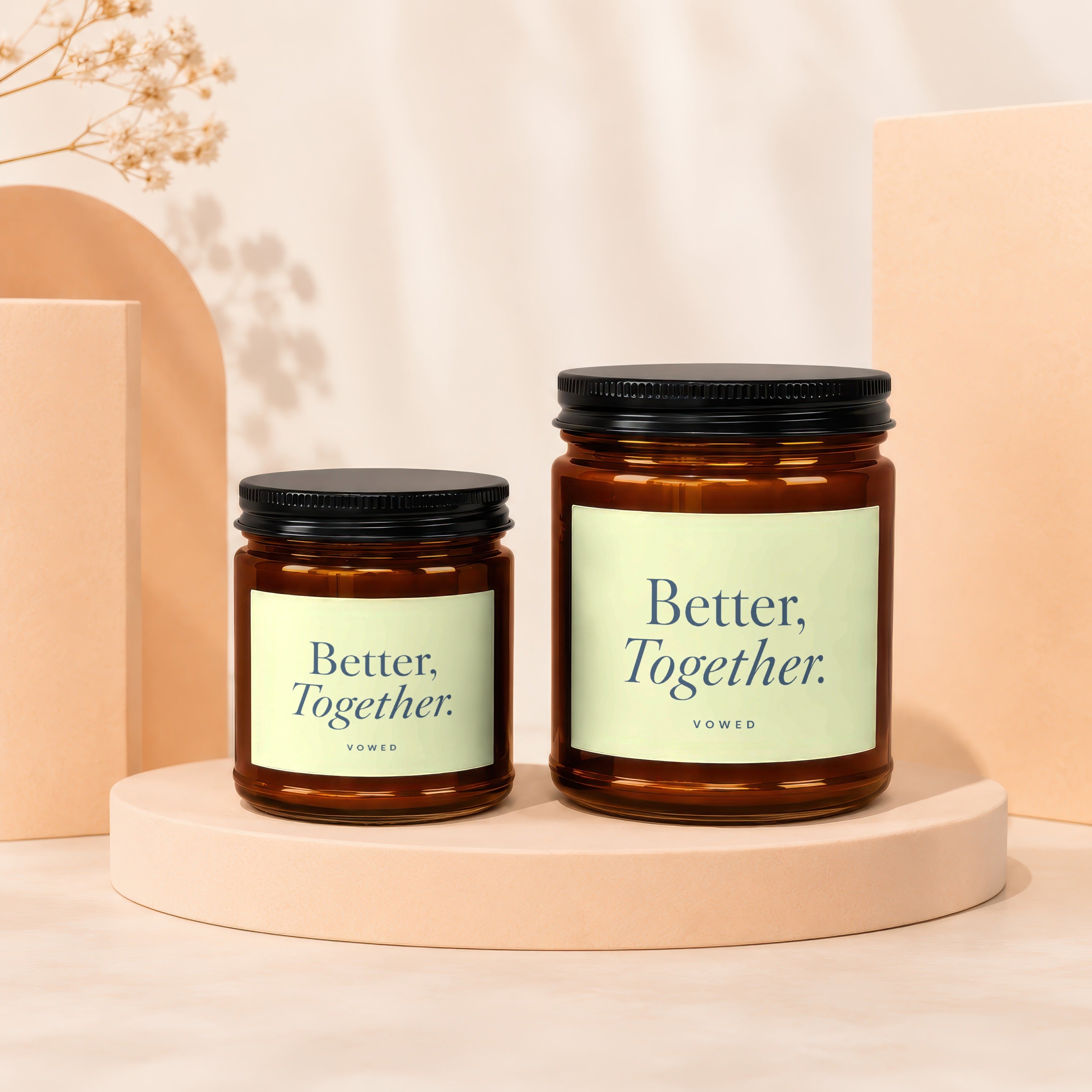 Two amber glass candles with black lids and light green labels stating "Better, Together."
