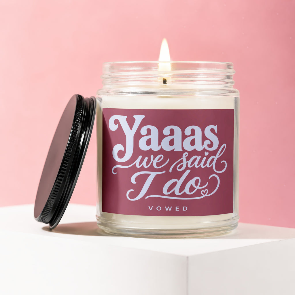 Glass jar candle with burning wick, lid off, and "Yaaas we said I do VOWED" text.