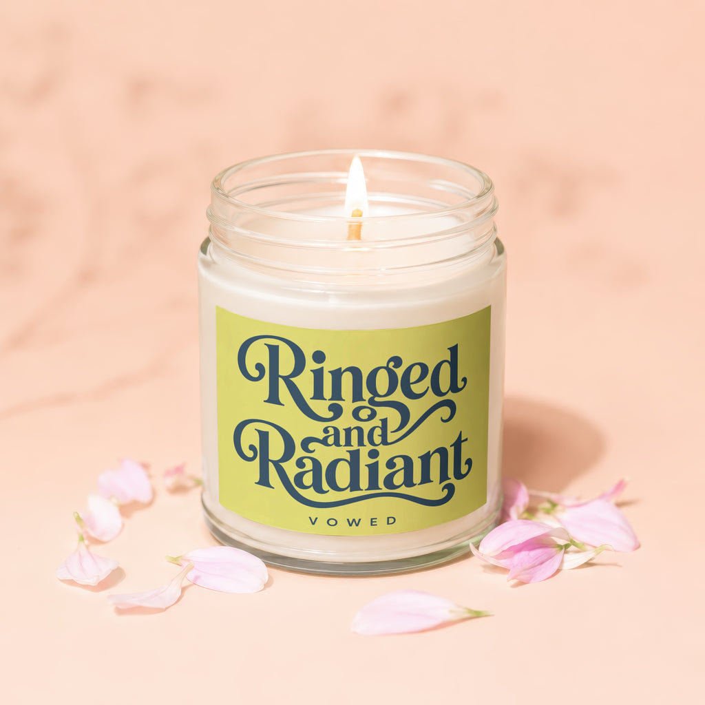 Candle with "Ringed and Radiant Vowed" text on a pale pink background with petals.