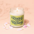 Candle with "Ringed and Radiant Vowed" text on a pale pink background with petals.