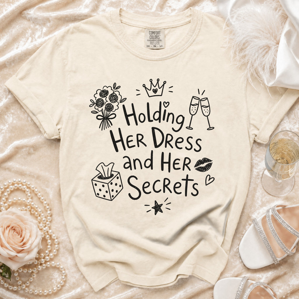 Cream graphic tee with "Holding Her Dress and Her Secrets" text and playful illustrations.