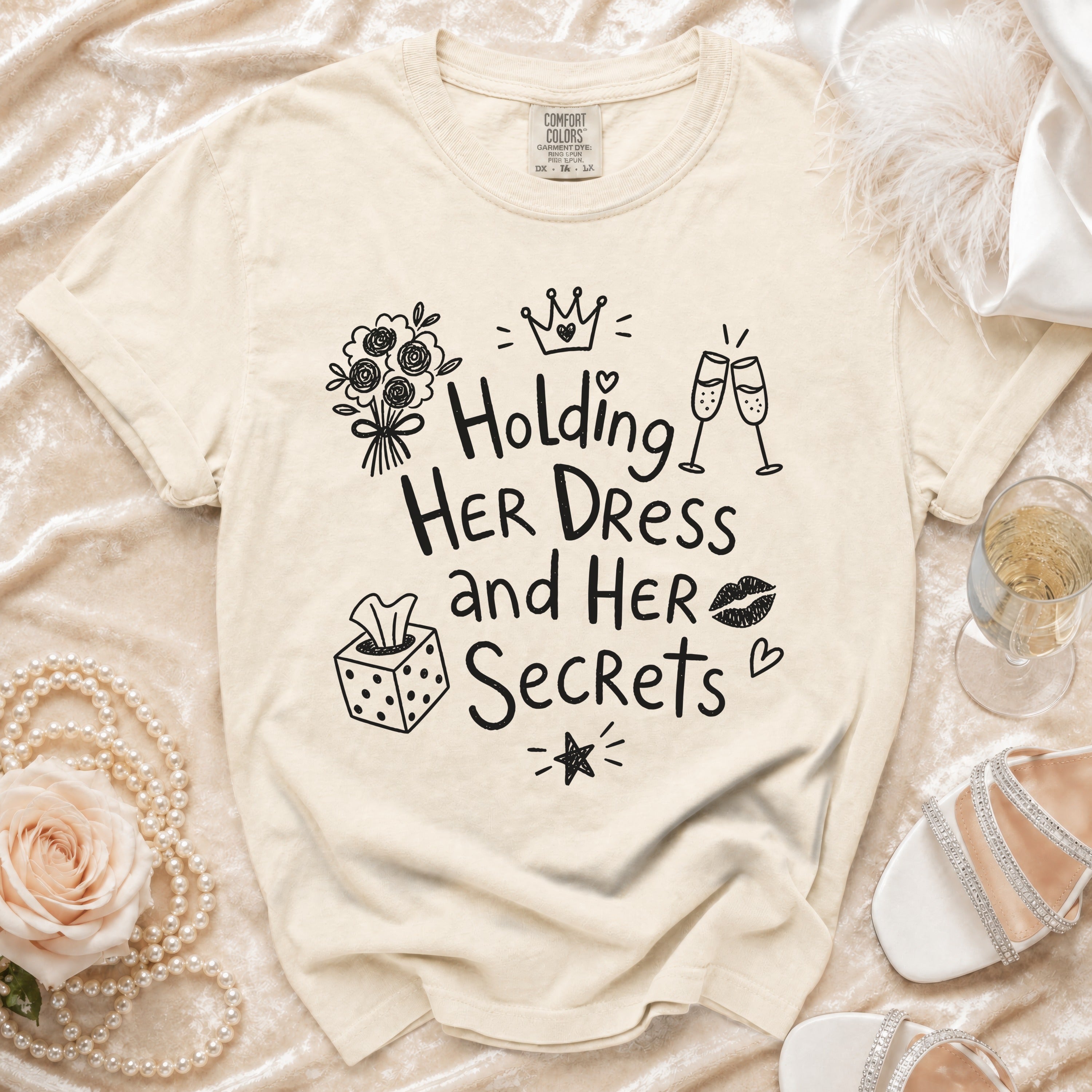 Cream graphic tee with "Holding Her Dress and Her Secrets" text and playful illustrations.