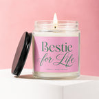 Glass candle with "Bestie for Life" label and lit wick on a pink background.