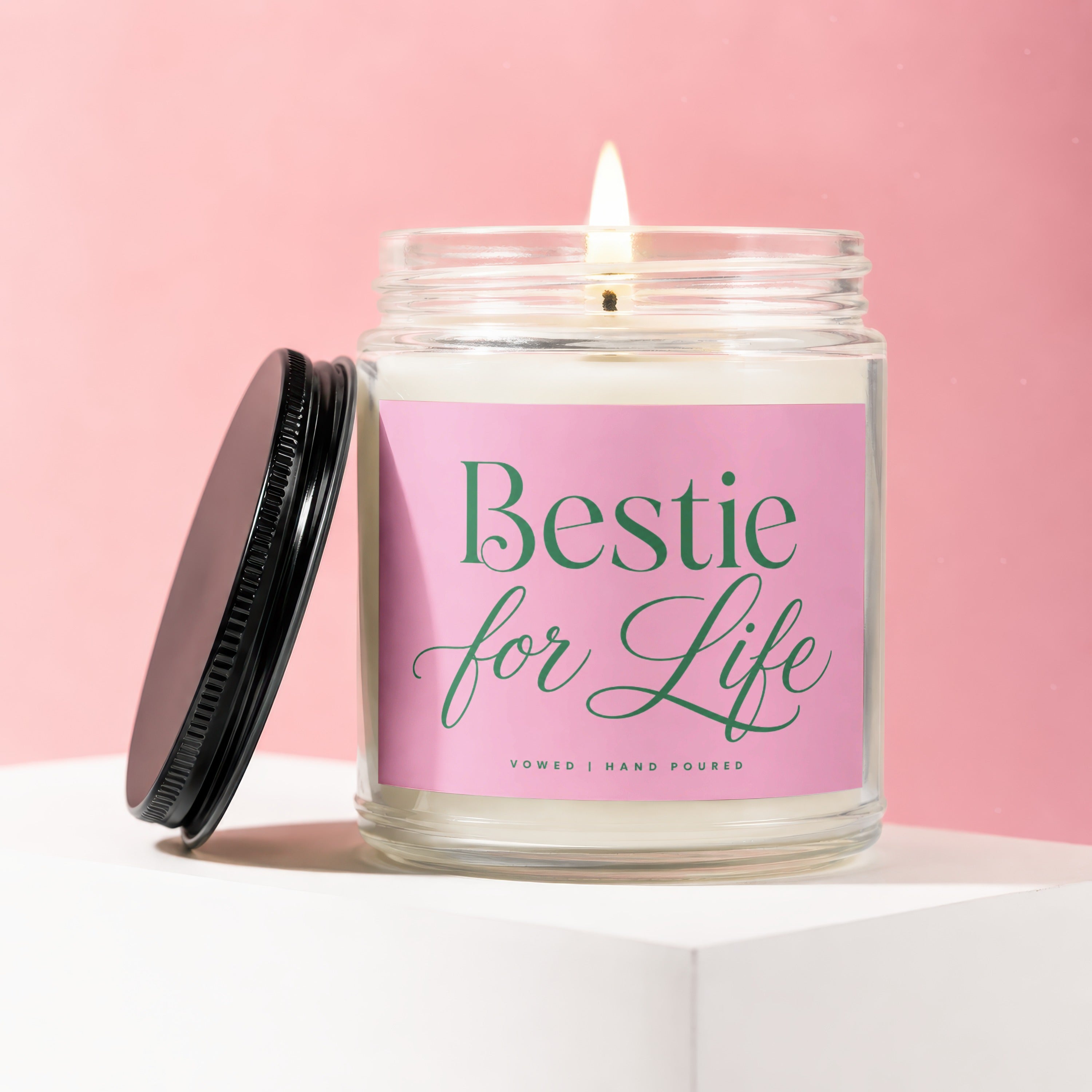 Glass candle with "Bestie for Life" label and lit wick on a pink background.
