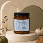 Amber candle with "Bride x Bride Vowed" text on label, displayed with decorative pumpkins and autumn leaves.