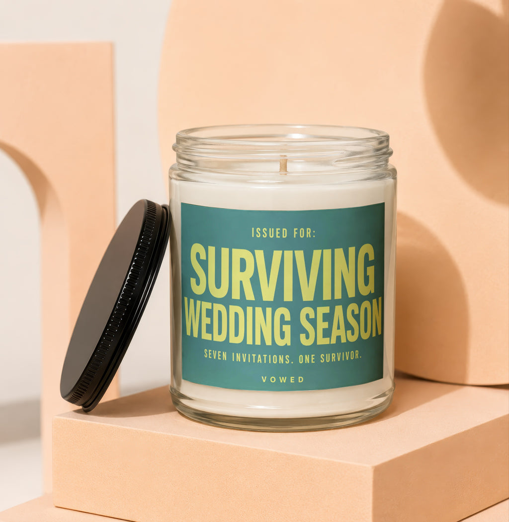 Glass candle with label reading "Surviving Wedding Season" with lid nearby.