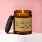 Lit amber glass candle with black lid, label reads "BOUND BY Moonlight vOWED".