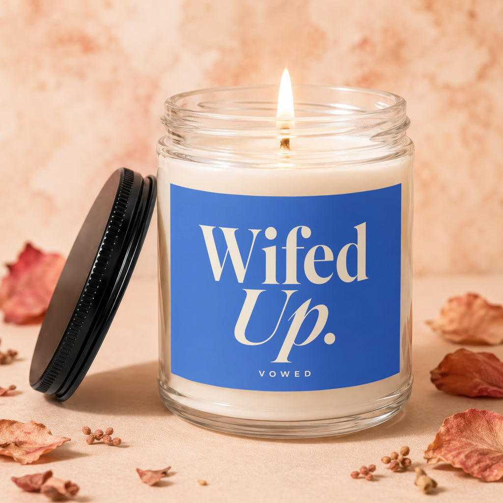 Glass candle burning with "Wifed Up. VOWED" on blue label, lid to the left.