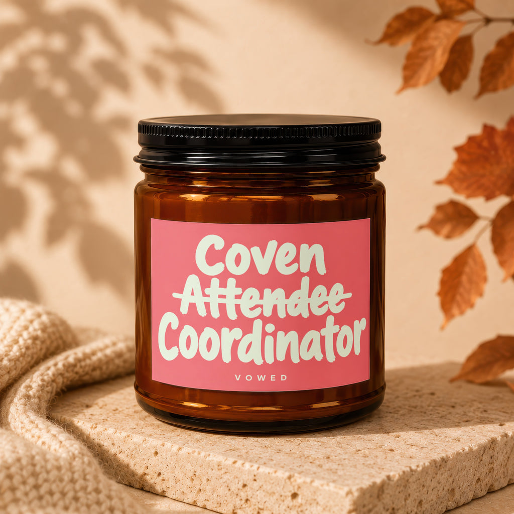 Amber jar candle with pink label reading "Coven Attendee Coordinator VOWED".